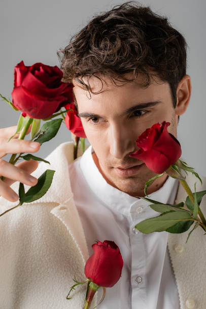 portrait of brunette man in white shirt and jacket near red fresh roses isolated on grey - Fotografie, Obrázek