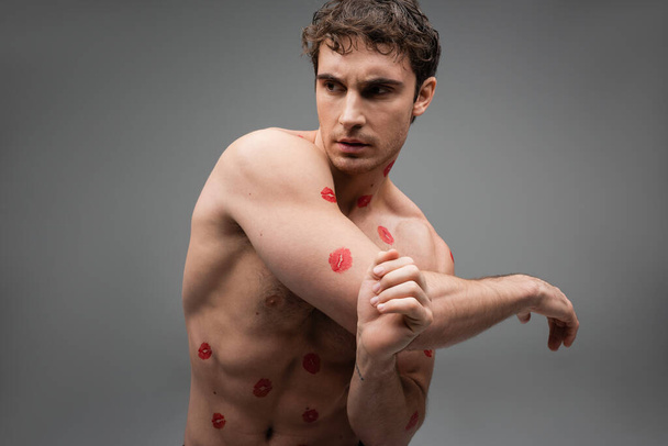 без сорочки і м'язистий чоловік з червоними слідами помади на тілі, що дивиться ізольовано на сірому
 - Фото, зображення