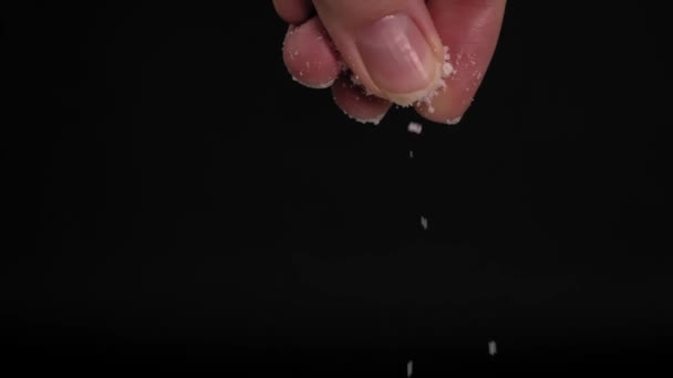 Slow-motion video of large female hand sprinkling or adding salt on black background to dish in kitchen. Black background slow motion. Kitchen or chef adds spices. - Materiał filmowy, wideo