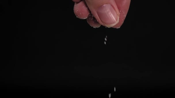 Slow-motion video of large female hand sprinkling or adding salt on black background to dish in kitchen. Black background slow motion. Kitchen or chef adds spices. - Metraje, vídeo