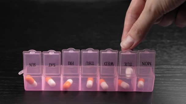 Woman's hand puts pills for week in pill dispenser. Concept of health care and medicines. course of treatment for week. . Storing scheduled doses of medications in box. - Imágenes, Vídeo