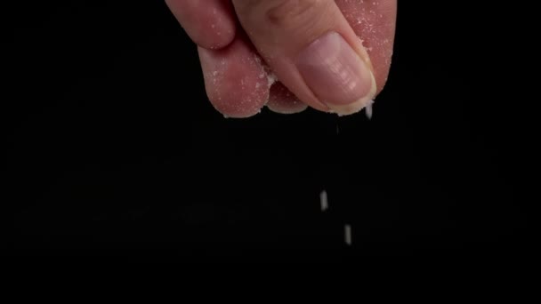Slow-motion video of large female hand sprinkling or adding salt on black background to dish in kitchen. Black background slow motion. Kitchen or chef adds spices. - Materiał filmowy, wideo
