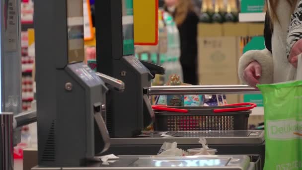 スーパーでセルフサービスのレジチェックアウトを使用している女性のバイヤー。顧客のスキャンは食料品店の自己で現金登録を役立つ使用して項目を生成する。キャッシャー端末の女性はオンラインで製品の支払い - 映像、動画