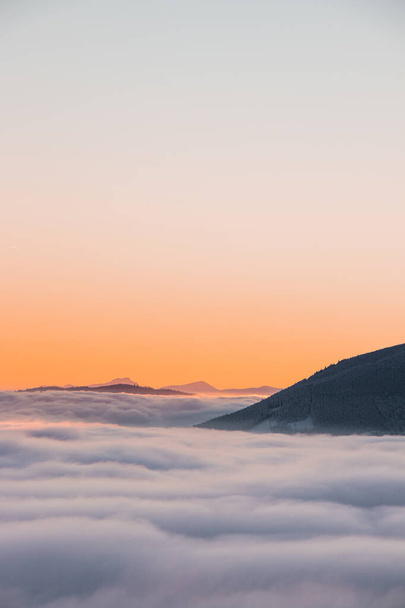 View of sea of clouds colored in the soft orange-pink hue of the morning sun. Peaks of the mountains rising out of this impermeable curtain. Sense of immortality and bliss. Beskydy, Czech republic. - Photo, Image