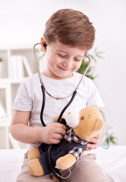 Adorable child with stethoscope of doctor examining teddy bear  - Фото, изображение