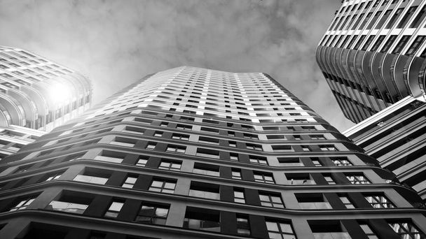 The narrow passage between modern residential buildings. Walls of high-rise apartment buildings and a narrow strip of sky between them. Modern urban living districts. Bottom view. Black and white. - Photo, Image