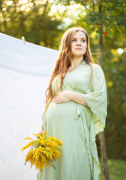 Pregnant woman with big belly, yellow Goldenrod Solidago flowers in hands. White female wears dress.Magic happy pregnancy. Childbirth preparations, emotional connection with baby. Baby shower Vertical - Foto, afbeelding