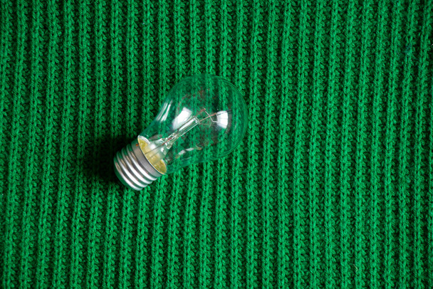 Μια λάμπα πυρακτώσεως βρίσκεται σε ένα πράσινο πλεκτό ύφασμα - Φωτογραφία, εικόνα