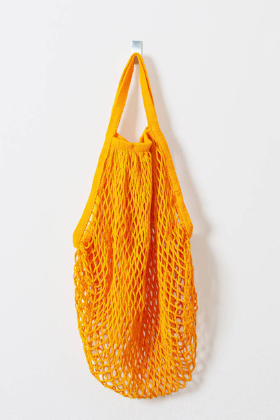mesh grocery bag. Reusable bag. Vegetarianism, raw food diet, conscious consumption, grid. orange mesh bag hanging on a hook. Next to the keys. Go shopping. - Foto, Bild