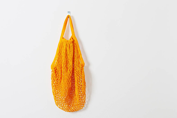 mesh grocery bag. Reusable bag. Vegetarianism, raw food diet, conscious consumption, grid. orange mesh bag hanging on a hook. Next to the keys. Go shopping. - Foto, Imagen