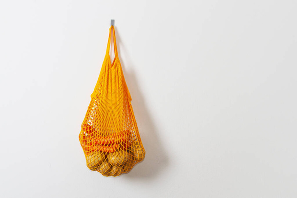 mesh grocery bag. Reusable bag. Vegetarianism, raw food diet, conscious consumption, grid. orange mesh bag hanging on a hook. Potato bag. Raw potatoes. - Foto, imagen