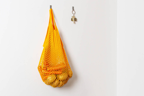 mesh grocery bag. Reusable bag. Vegetarianism, raw food diet, conscious consumption, grid. orange mesh bag hanging on a hook. Potato bag. Raw potatoes. - Fotó, kép