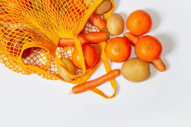 Orange mesh bag. View from above. Fresh vegetables and fruits from the farmers' market. Raw potatoes, raw carrots, apples, tangerines, oranges. Conscious consumption, reusable bag, string bag. Vegetarianism, raw food diet, ecology, fresh vegetables.  - Fotografie, Obrázek
