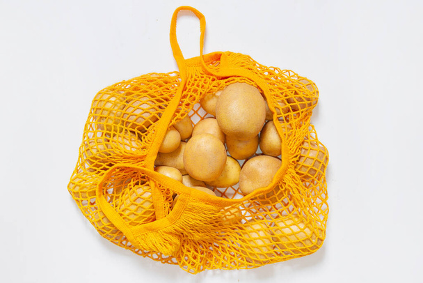 Mesh reusable bag with fresh potatoes. Orange string bag. Raw potatoes. View from above. Vegetarian, raw food, fresh vegetables. Conscious consumption. Without plastic. Recycling. - Fotografie, Obrázek