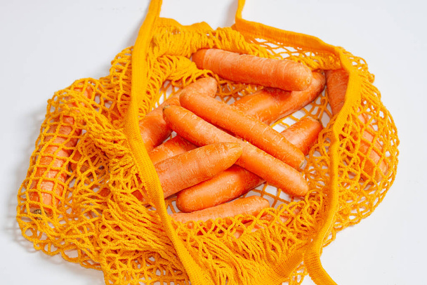 Mesh reusable bag with fresh carrots. Orange string bag. Raw carrots. View from above. Close-up. Vegetarian, raw food, fresh vegetables. Conscious consumption. Without plastic. Recycling. - Foto, Bild