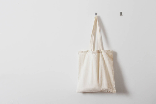 White rag bag for groceries. Reusable bag. Vegetarianism, raw food diet, conscious consumption, tissue. Hanging white fabric bag on a hook - Fotografie, Obrázek