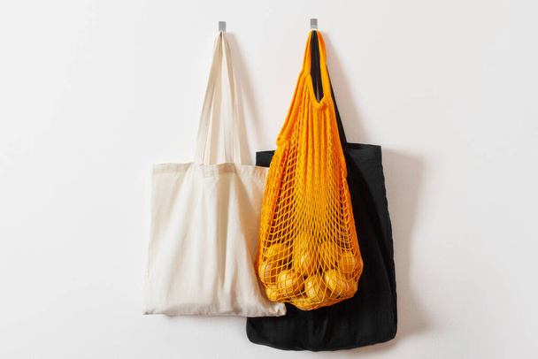 mesh grocery bag. Reusable bag. Vegetarianism, raw food diet, conscious consumption, grid. orange mesh bag hanging on a hook. Several shopping bags. White, black, yellow. Raw potatoes - Foto, Bild