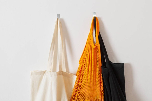 mesh grocery bag. Close-up of bag handles. Reusable bag. Vegetarianism, raw food diet, conscious consumption, grid. orange mesh bag hanging on a hook. Several shopping bags. Black, yellow, white - Foto, Bild