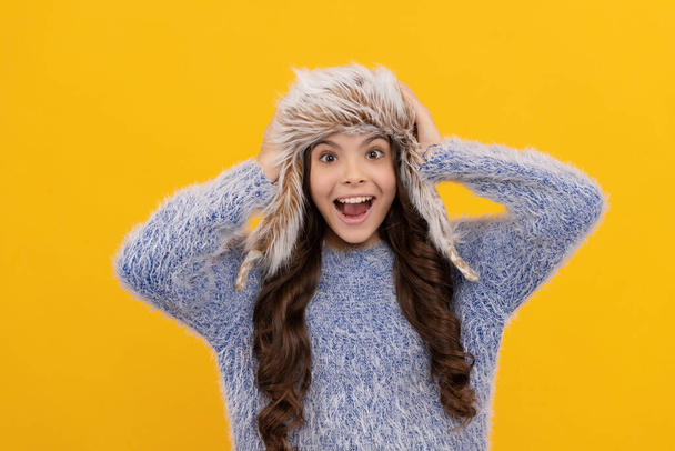 female fashion model. teen girl in knitwear on yellow background. portrait of child wearing warm clothes. express positive emotion. winter fashion. amazed kid with curly hair in earflap hat. - Foto, afbeelding