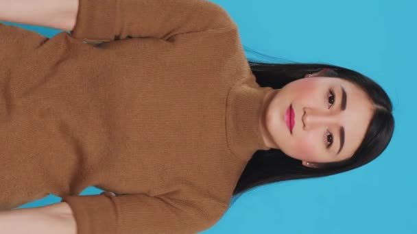Вертикальное видео: азиатская горничная улыбается в камеру, надевая резиновую перчатку после уборки дома, стоя в студии. Домработница была умелой в искусстве ведения домашнего хозяйства, обеспечивая каждую поверхность - Кадры, видео
