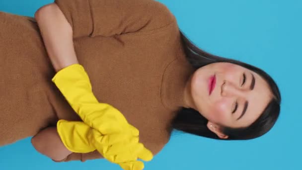 Вертикальне відео: Посміхнена азіатська покоївка плескає руки перед камерою після закінчення прибирання, стоїть у студії над синім фоном. Господиня дуже пишається своїм домашнім господарством. - Кадри, відео