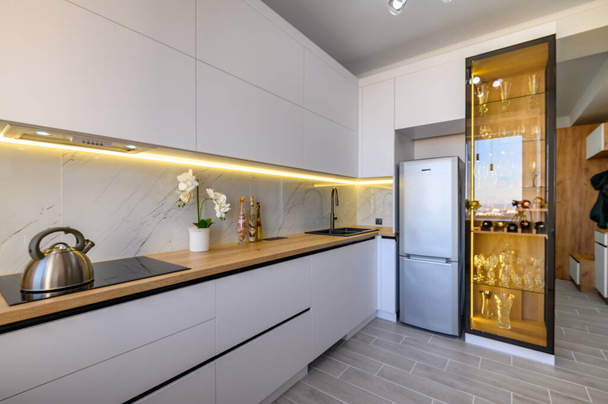 Ένα κομψό λευκό στούντιο διαμέρισμα με μια πλήρως εξοπλισμένη κουζίνα και ένα κομψό γυαλί μπουφέ - Φωτογραφία, εικόνα