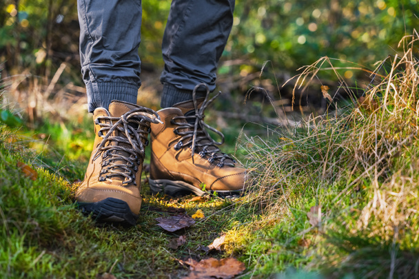 Αγνώριστο αρσενικό ταξιδιώτη ή πεζοπόρος που περπατά στο δάσος και σκαρφαλώνει στο λόφο. Κοντινές μπότες πεζοπορίας από την μπροστινή πλευρά. Ηλιόλουστο δάσος - Φωτογραφία, εικόνα