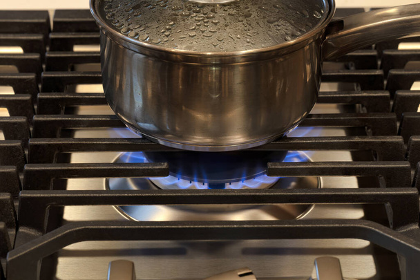 Сучасна кухонна плита готується зверху з сковородою. Газове полум'я крупним планом на газовій печі з металевим грилем
 - Фото, зображення