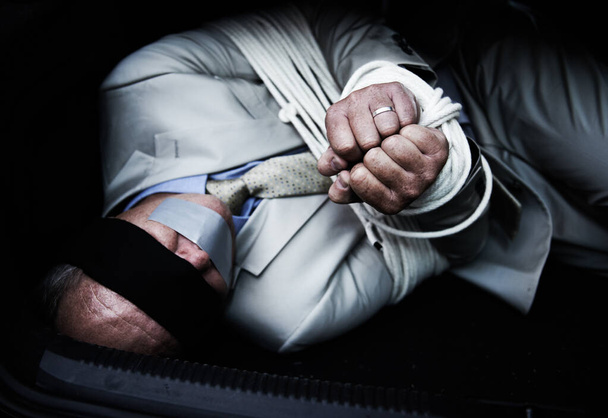 Один и напуган. Завязанный и с завязанными глазами бизнесмен, лежащий в багажнике машины - Фото, изображение