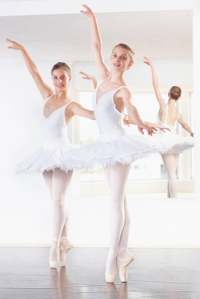 Танцует в идеальном единстве. Полнометражный снимок двух балерин, практикующихся в студии с зеркалом позади них - Фото, изображение