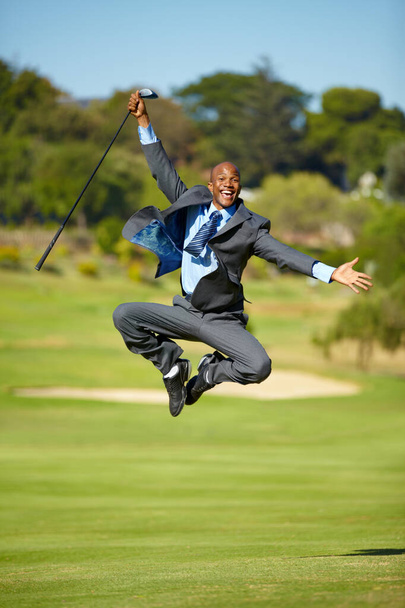 Επιτυχία στις επιχειρήσεις και στον αθλητισμό. Ένας Αφροαμερικάνος επιχειρηματίας που πηδάει χαρούμενα στον αέρα σε ένα γήπεδο γκολφ. - Φωτογραφία, εικόνα