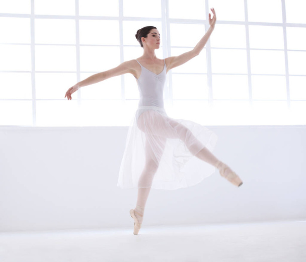 Elegance and grace are her goals. Graceful young ballerina in white dancing en pointe - Fotografie, Obrázek
