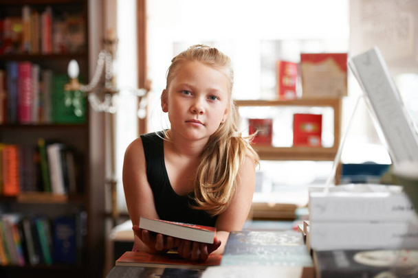 She comes to the library once a week. Portrait of a cute blonde girl standing with a book in the library - Foto, Imagem