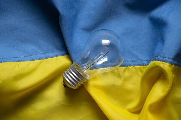 На прапорах України лежить лампа розжарювання, люди без світла в Україні через російські ракетні атаки, війну, кризу. - Фото, зображення