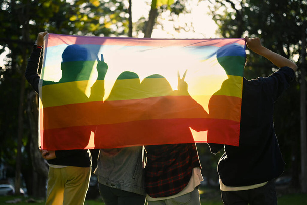 Group of young activist with pride rainbow flag on foreground, supporting LGBTQ pride. LGBT community concept. - Foto, Bild