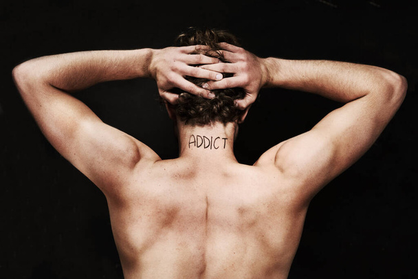 Branded as an addict. Rear view of a naked young man holding his head with the word addict on the back of his neck - Foto, immagini