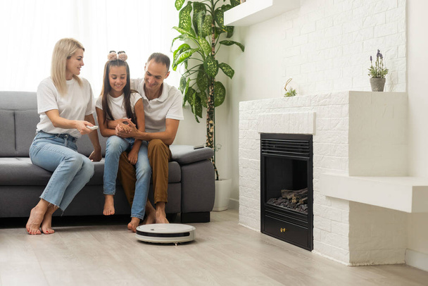 Family resting while robotic vacuum cleaner doing its work at home. - Photo, Image