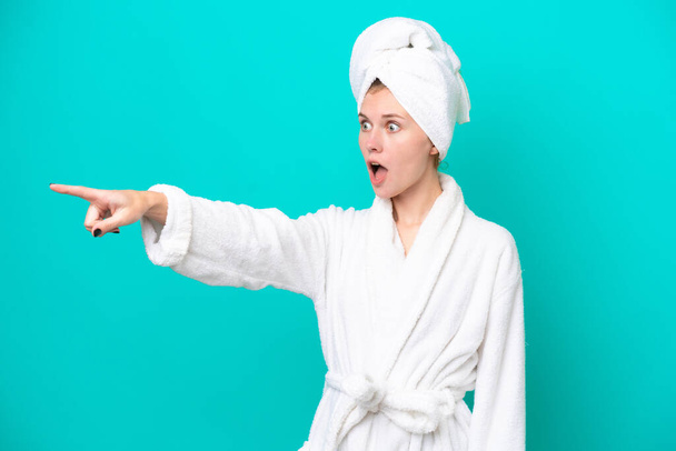 Young woman in a bathrobe isolated on blue background pointing away - Fotó, kép