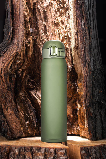 Promotional photo of the bottle. Photo of a thermos. Beautiful photo of a thermal bottle. Thermos and flask. Thermos of olive color against the background of tree bark. - Foto, Bild