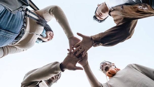 Low angle view of a A group of mulitethnic group of students join hands to form a team - Fotoğraf, Görsel