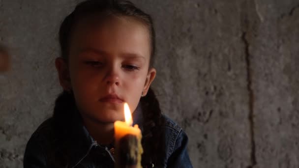 A small child sits in the basement with a candle, rocket attacks on Ukrainian cities. Upset child. War in Ukraine. Energy blackout - Video, Çekim