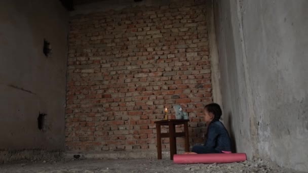 A small child sits in the basement with a candle, rocket attacks on Ukrainian cities. Upset child. War in Ukraine. Energy blackout - Materiał filmowy, wideo