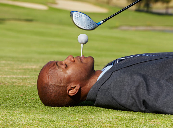 I trust my business partners. Concept shot of an african american businessman lying on a green with a tee in his mouth and a club hovering over him - Foto, imagen