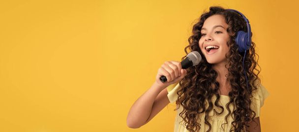 cheerful teen girl listen music in headphones and singing in microphone, vocal school. Child portrait with headphones, horizontal poster. Girl listening to music, banner with copy space - Photo, Image
