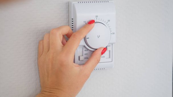 Woman hand adjusts or turns on wall temperature controller controller button. Climate control in room - Fotoğraf, Görsel