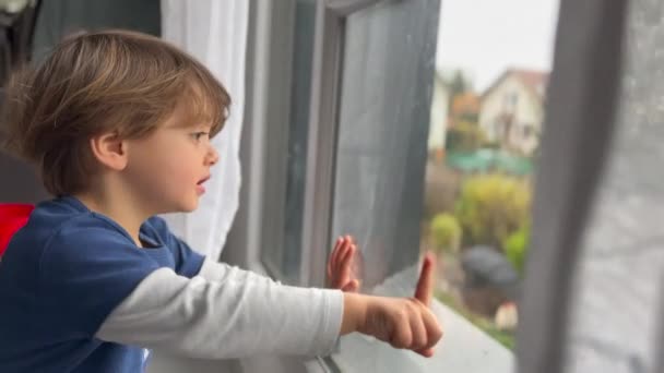 Child stuck at home sitting by window. Little boy wanting to go outside points hand outdoors. - Filmagem, Vídeo