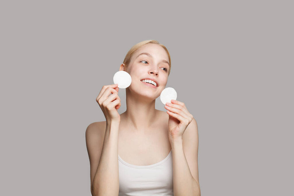 Portrait of a beautiful young woman cleaning her face with cotton pads, removing makeup. Beauty and spa concept - Foto, Imagen