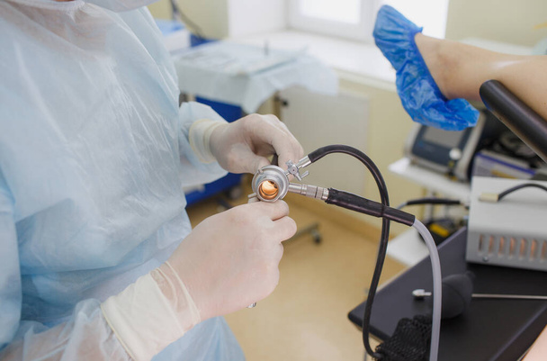 Ένας άνδρας γιατρός με λευκό παλτό και λαστιχένια γάντια, κρατώντας ένα κολονοσκόπιο σε ένα μπισκότο, ετοιμάζεται για χειρουργική επέμβαση. - Φωτογραφία, εικόνα