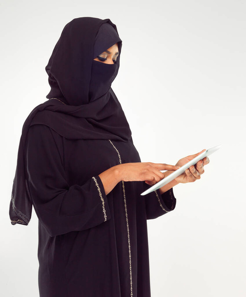 Женщина, скрижаль и хиджаб мусульман для онлайн-исламистских исследований на белом фоне студии. Женщина, стоящая с сенсорным экраном с шарфом читает новости об исламе, арабском языке или культуре. - Фото, изображение