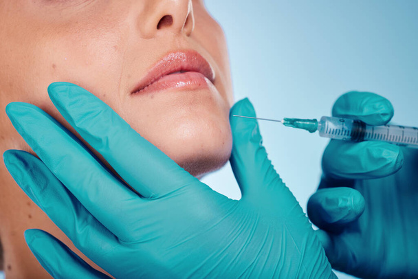 Botox, hands and cosmetic surgery with a woman and doctor in studio on a blue background for face change. Beauty, skin and injection with a surgeon holding a syringe for female client facial filler. - Foto, Bild